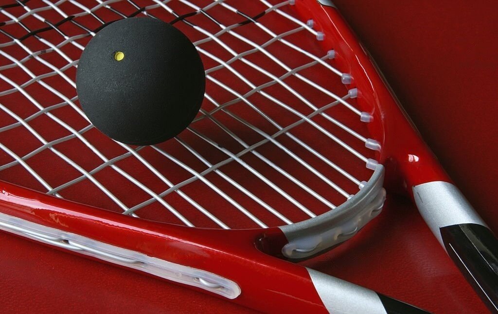 A red squash racket with a ball resting on top, set against a red background.