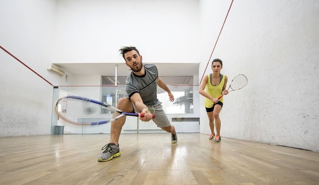 A man and a woman engaged in a squash match, both holding rackets and focused on the game.