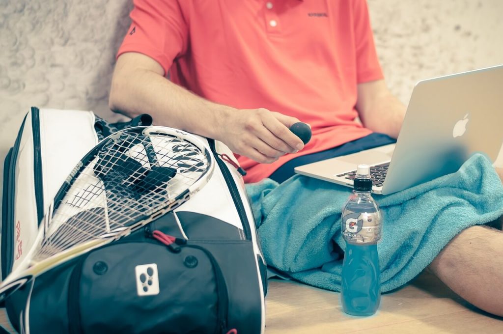 Person sitting with laptop and squash gear, including a squash ball.